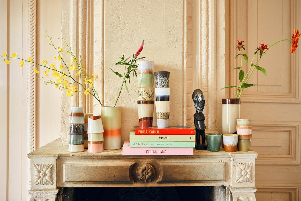 books, vases and a small sculpture on a fire place mantel filled with stacks of stoneware coffee cups