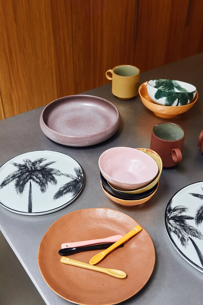 table with a brown side plate, yellow and pink porcelain teaspoons and bowls and plates in different colors and patterns