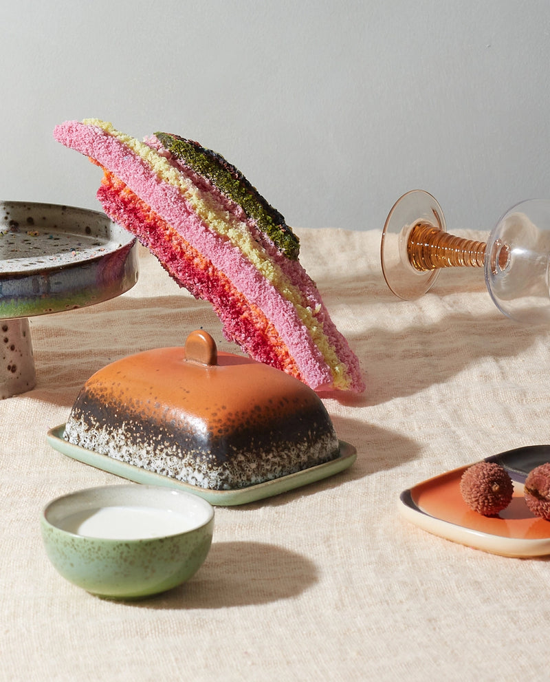 retro style stoneware butterdish in orange brown and green on a table with cake in multiple colors