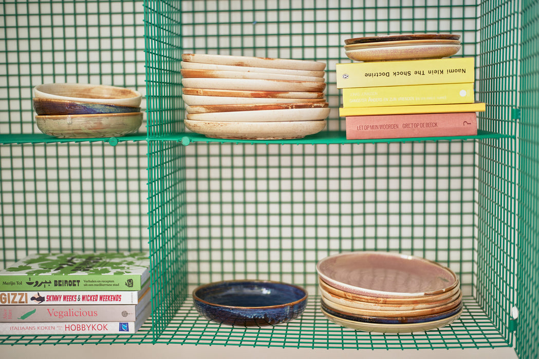 green open shelving unit with a stack of porcelain cream and brown colored dinner plates and books
