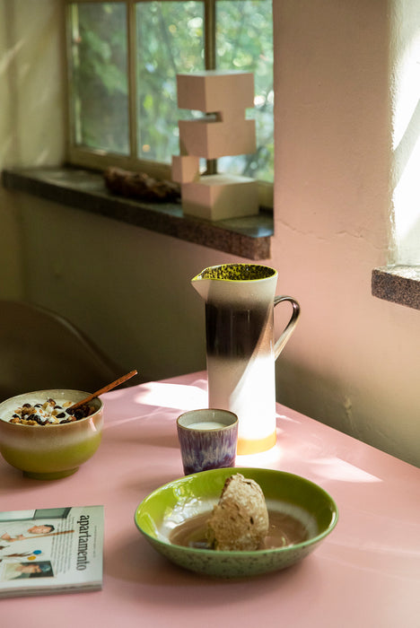 tall stoneware pitcher with orange, white and brown finish on a pink breakfast table with green colored bowls