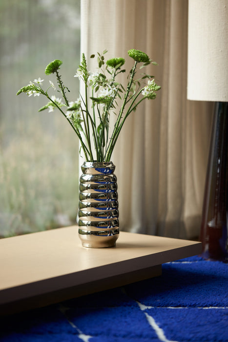 shiny chrome colored flower vase on a low table and blue rug
