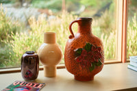 cappuccino brown colored round flower vase in a window setting next to a retro orange vase and small dark brown vase