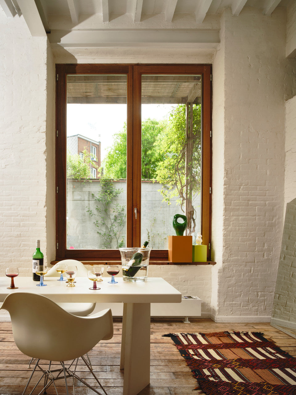 dining area with a large white table filled with glasses with colored stems and a glass wine cooler with a bottle of wine