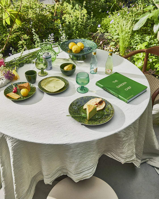 outdoor table with linen table cloth, green colored tableware and a glass teaspoon with a twisted handle