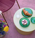 green stoneware side table on a purple floor with 3 green glass plates with fruit and a croissant