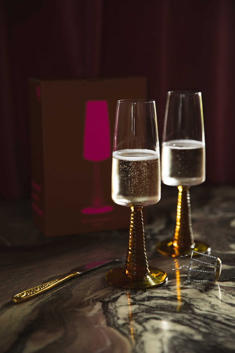 two champagne glasses with ochre colored stem filled with bubbly