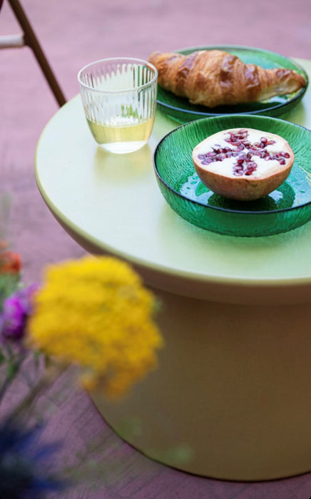 green stoneware side table on a purple floor with 3 green glass plates with fruit and a croissant