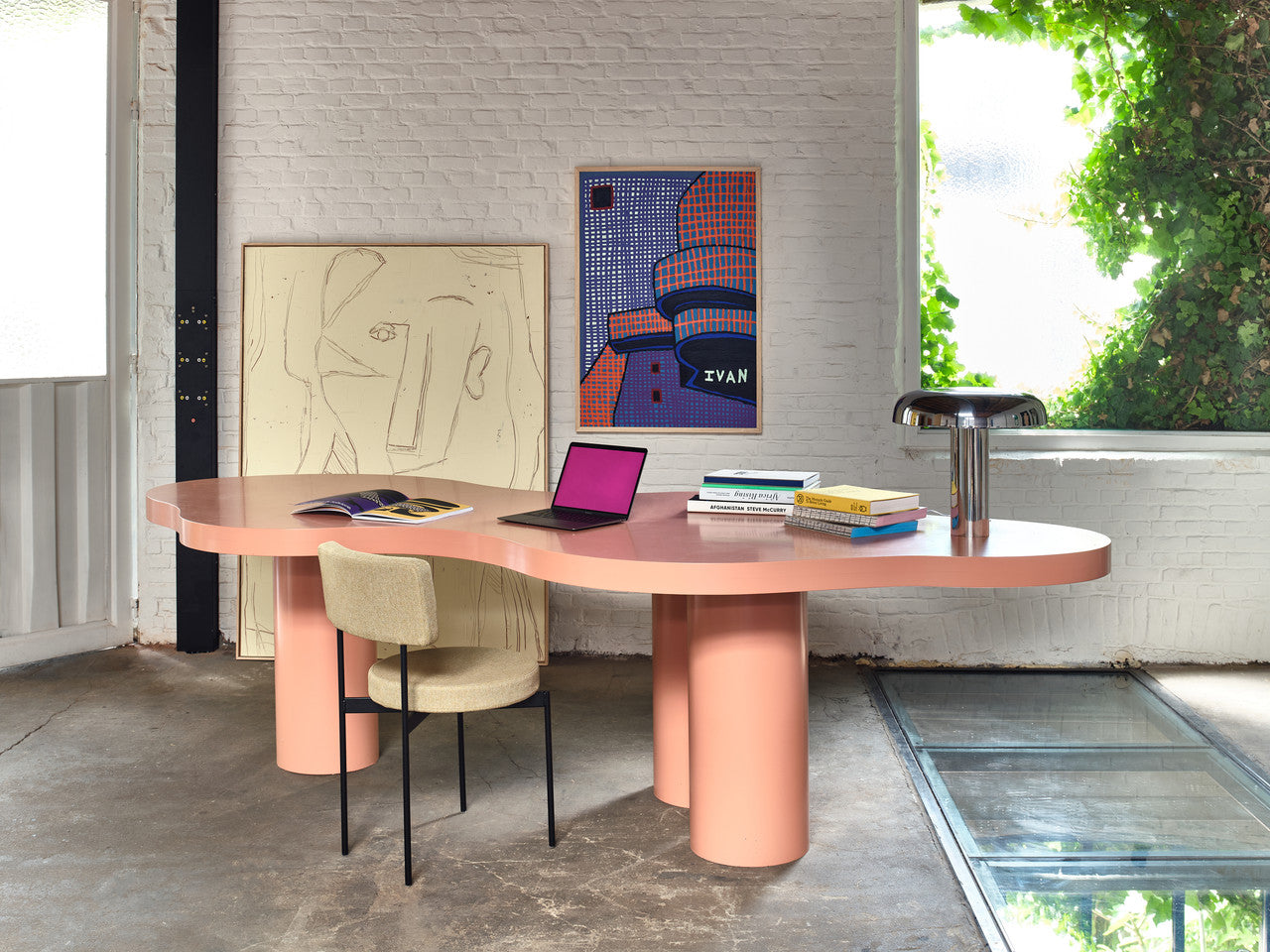 large abstract painting called visage standing against a white wall behind an organic shaped peach colored desk