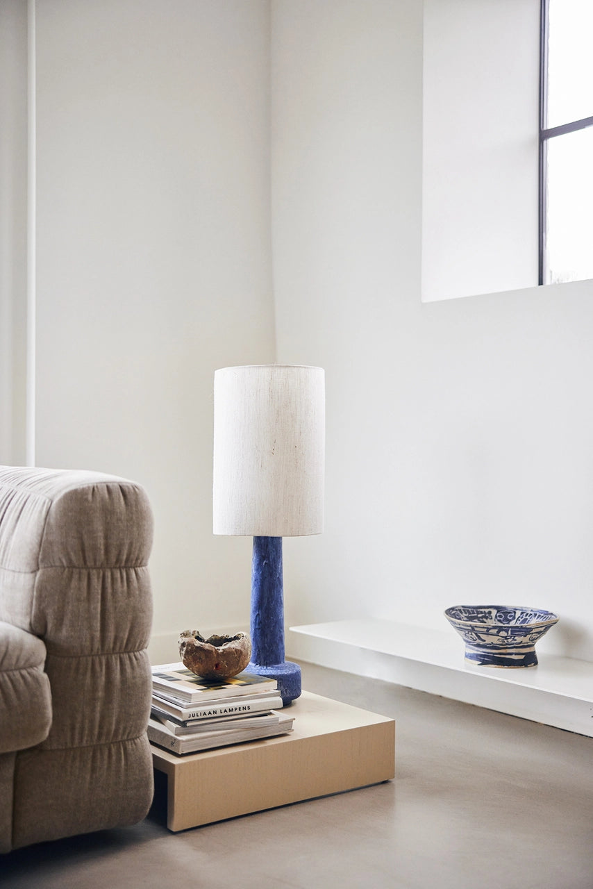  sand colored wooden low plateau table next to a linen couch with a blue table lamp