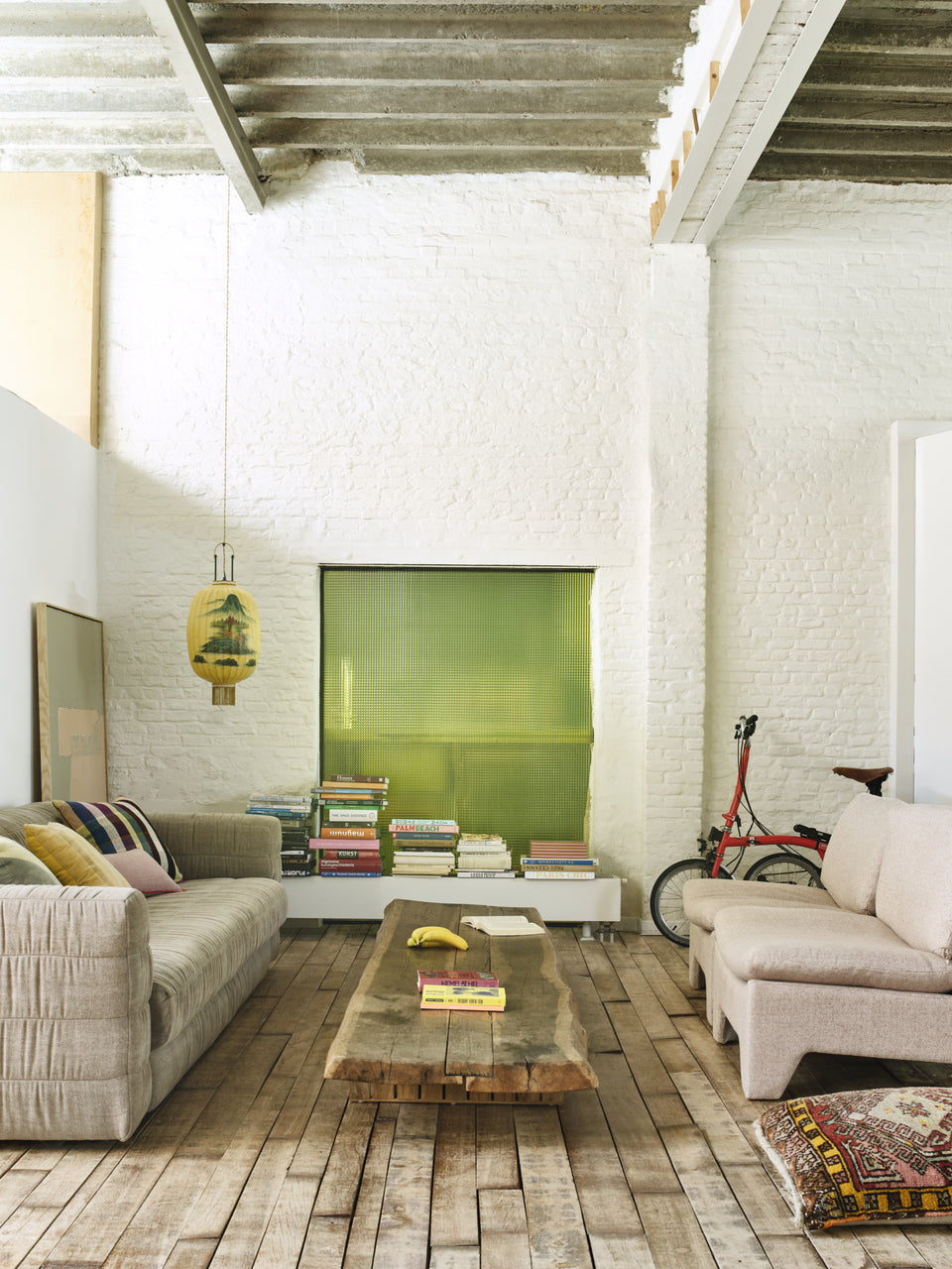 loft with white painted exposed brick wall, a linen taupe colored sofa, large coffee table in the middle and two retro style lounge chairs with a blush mélange fabric