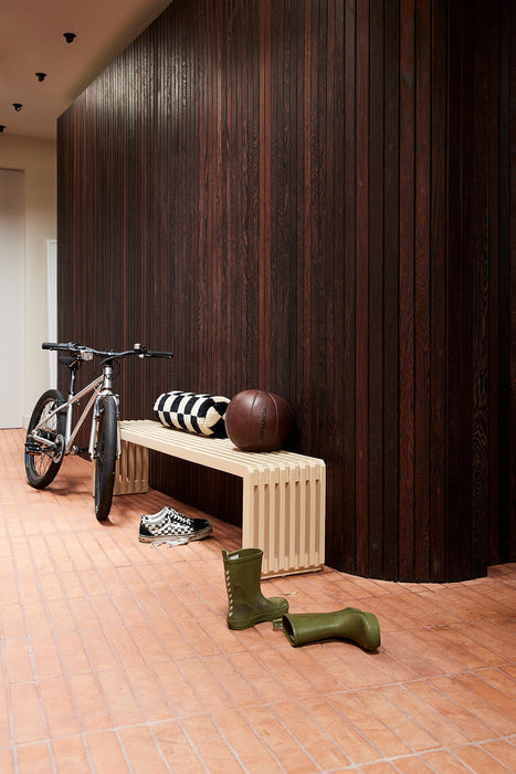 sand colored slatted bench against brown wooden wall with bike and boots