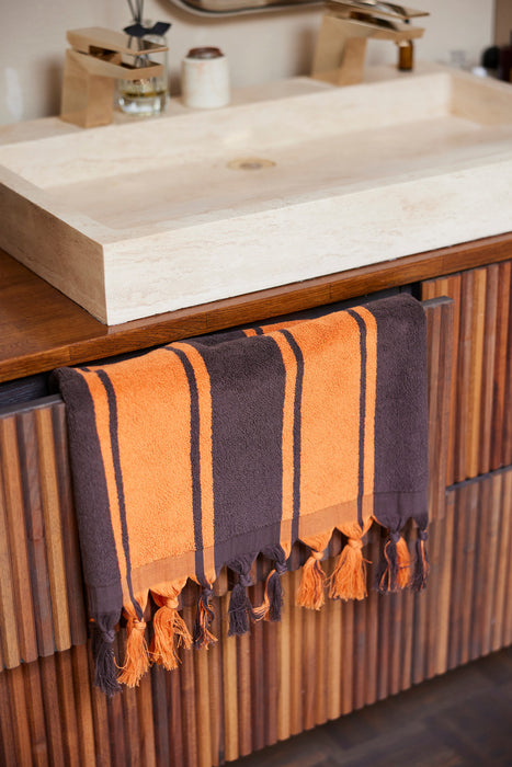 brown and orange striped large towel with fringes under a bathroom sink