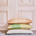 3 large hand woven woolen lumbar pillows with green and white piping on a stack against a wooden wall