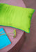 textured yellow and green accent pillow on pink table with yellow flower and blue book