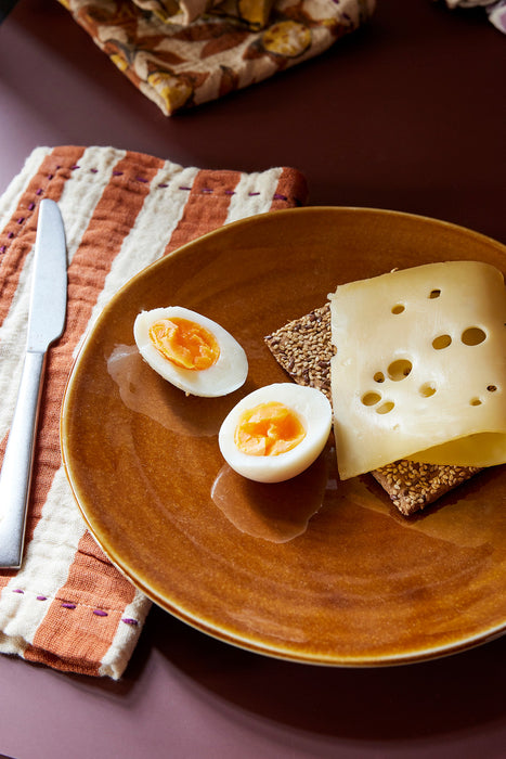 tangerine and white striped napkin next to a brown plate with an egg and a slice of bread with cheese