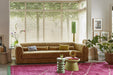ochre velvet long club couch and a large pink woolen rug with green tassels and two different shaped green accent tables