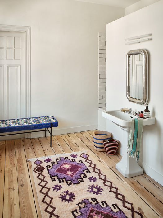 large cotton bohemian style bat rug with purple hues on wooden floor in bathroom