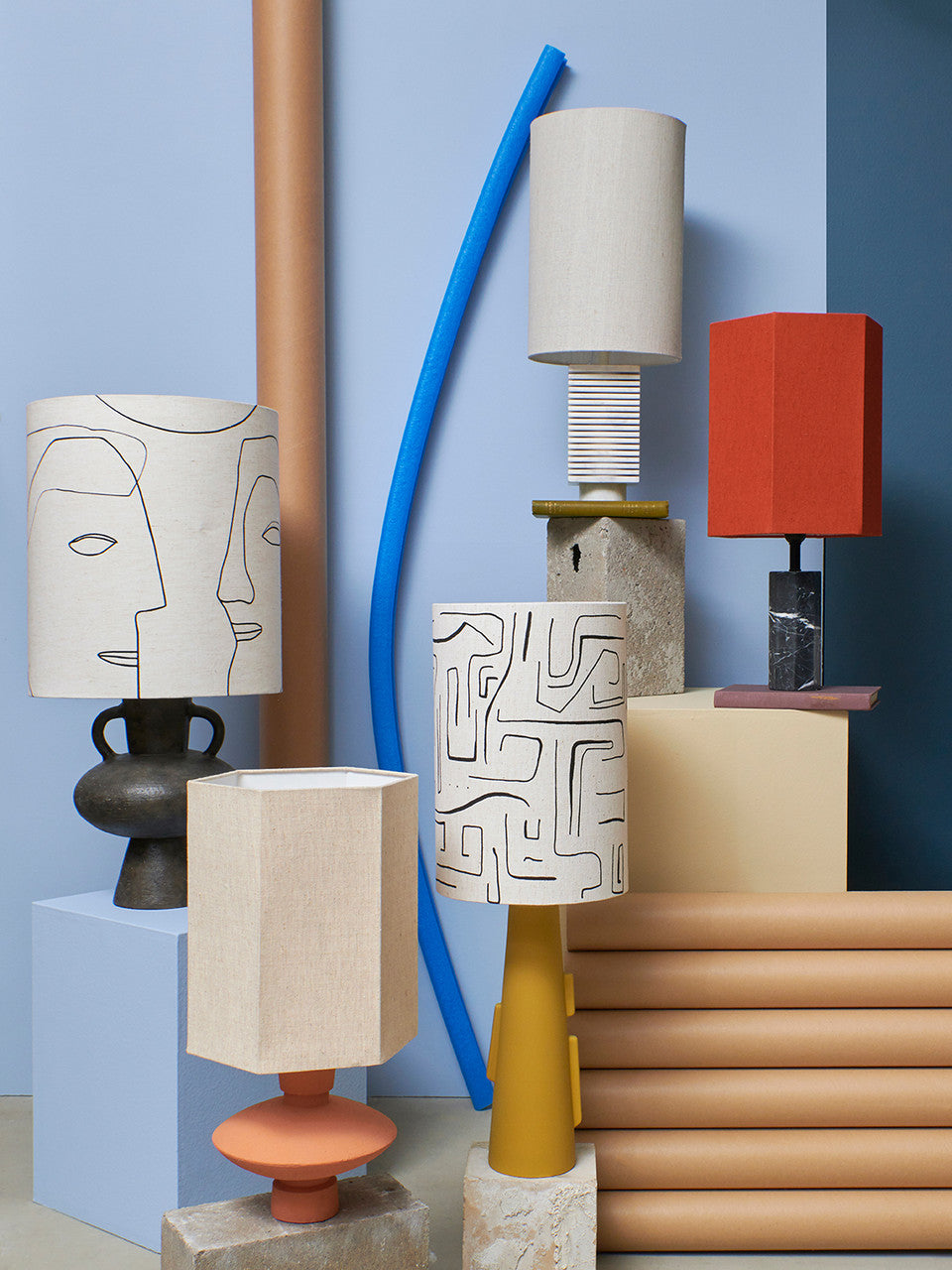 charcoal, teracotta, mustard yellow and black and white marble table lamps with natural linen shades on a display against a blue wall