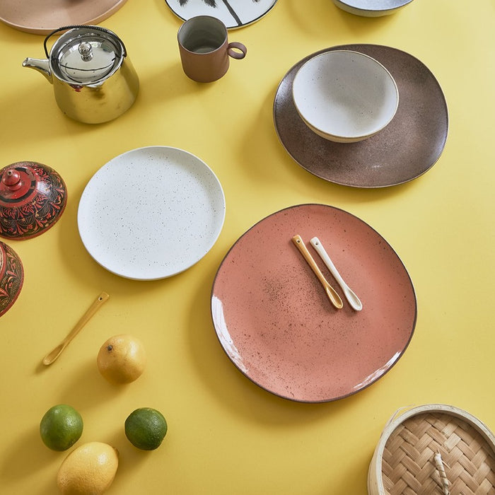 yellow countertop with ceramic plates in cherry, white and brown tones and a set of ceramic teaspoons in pastel colors