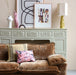 retro style brown corduroy sofa with mustard green table lamp with hexagon shape shade on a soft green fireplace mantel 
