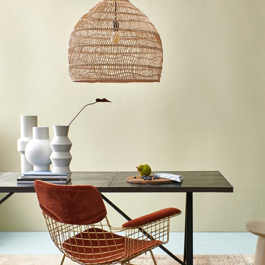 wicker basket light hanging above a black table with a brass dining chair with velvet covering