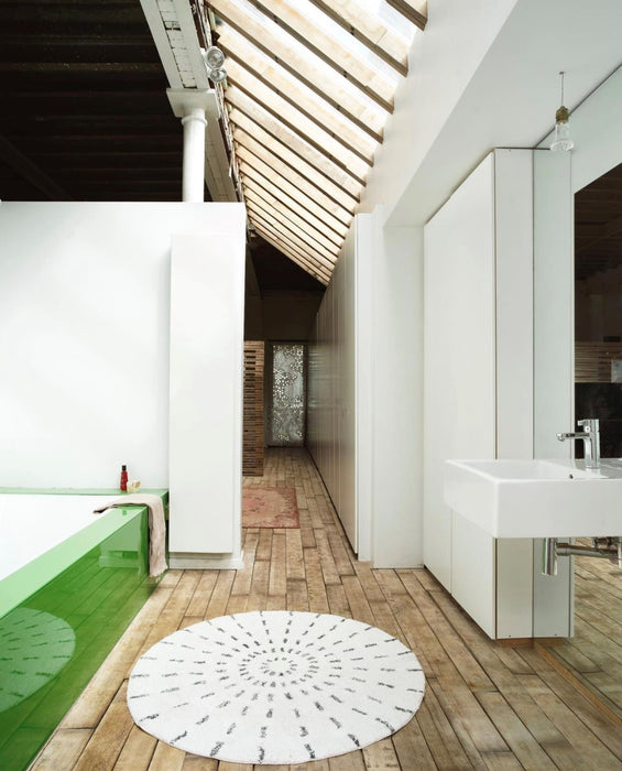 bathroom with high ceilings, a wooden floor a green bathtub and a round black and white bath mat
