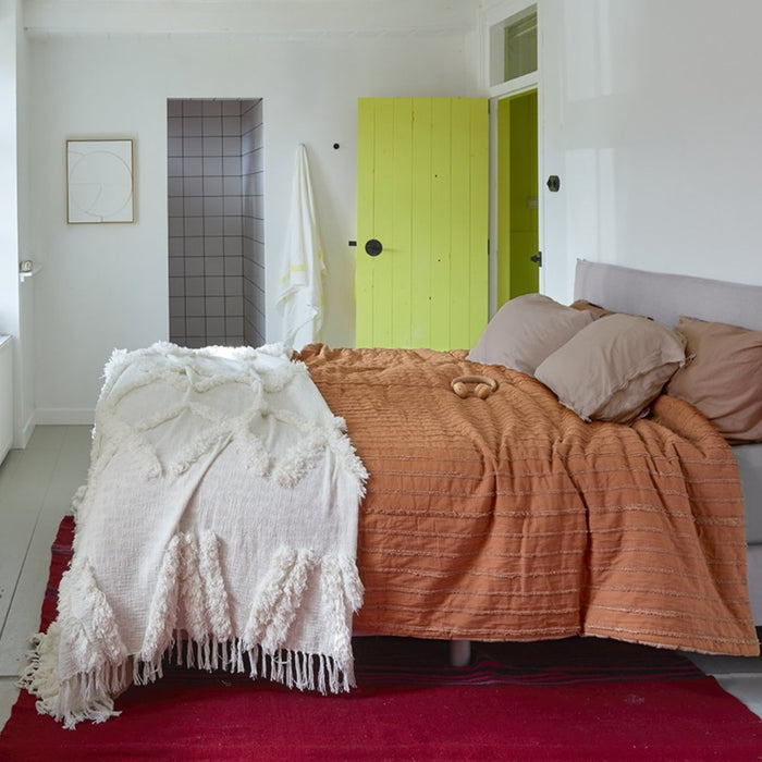 bedroom with an orange/terra color bedspread and a yellow door and a grey bathroom