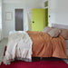 bedroom with an orange/terra color bedspread and a yellow door and a grey bathroom