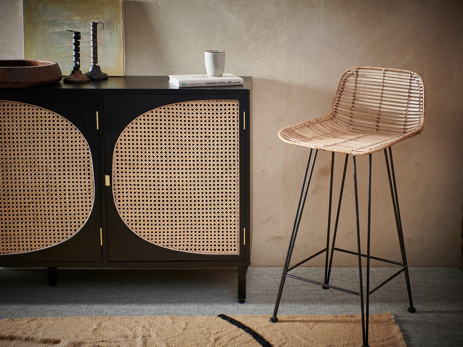 black wooden and cane webbing sideboard next to a natural rattan handwoven counter stool
