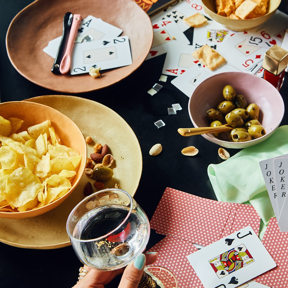 potato chips in orange bowl, yellow plate with nuts and pink bowl with green olives and a yellow ceramic spoon