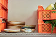 handmade, moss green ceramic deep plate in an open shelving rack next to an orange crate with vegetables