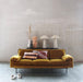 ochre velvet sofa with striped pillows and two triangle shaped cone table lamps against a grey, concrete wall
