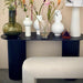 natural linen upholstered bench in front of a console table filled with white and green flower vases