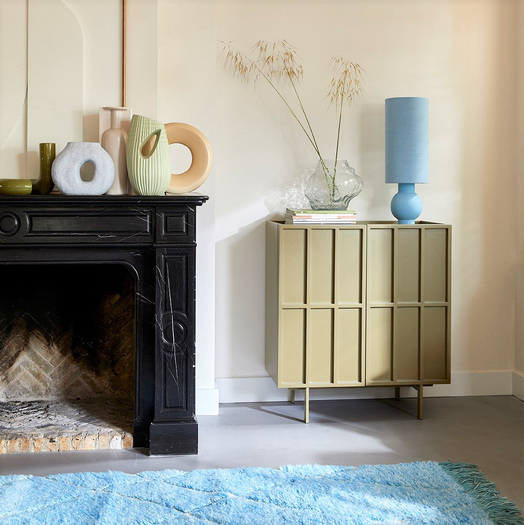 living room with credenza and blue table lamp with tall shade next to a cloud shaped glass flower vase with 3 stems