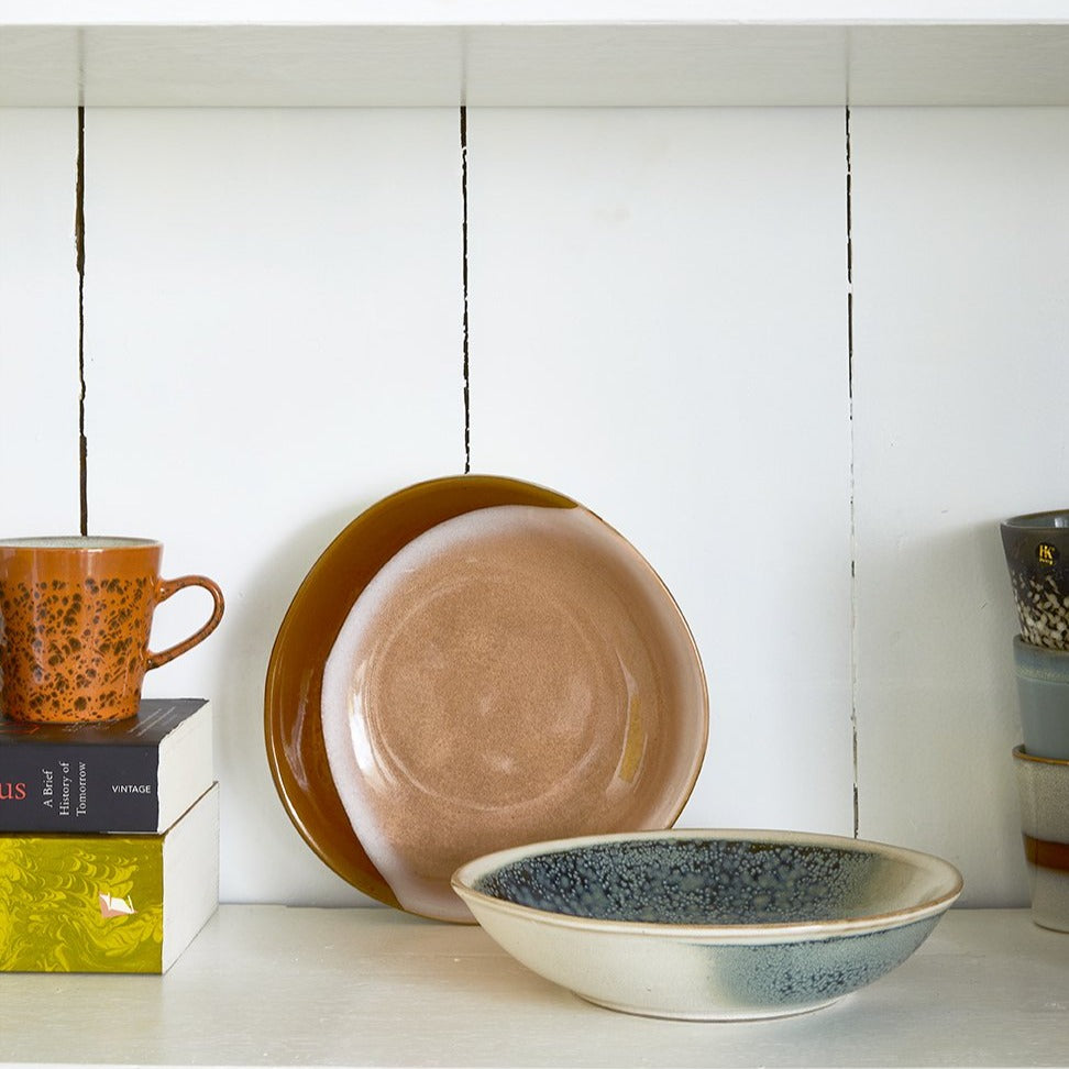 curry bowl in earth tones in an open shelving cabinet behind a curry bowl in blue and green tones