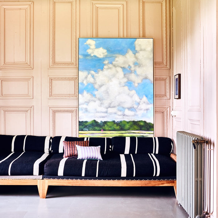 sofa with black and white striped fabric and a large  painting with clouds in the sky and a pink chair on grass