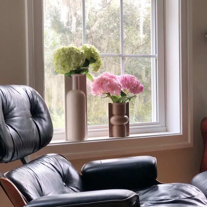 Eames chair in front of window that states two mold vases in clay colors with flowers