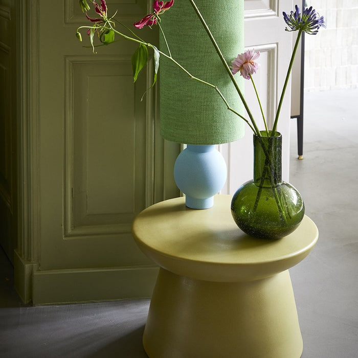 detail of earthenware accent table in green with green glass vase and blue and green table lamp