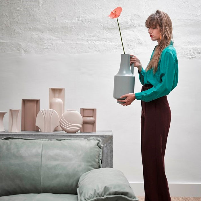 green sofa, clay colored vases and a woman holding a big green vase with one handle