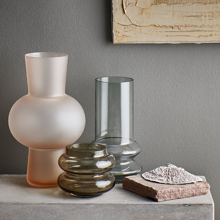a frosted peach colored glass vase, brown colored glass vase and grey colored glass flower vase on a concrete tabletop