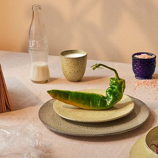 yellow ceramic speckled cup with milk and a green pepper on a yellow ceramic side plate