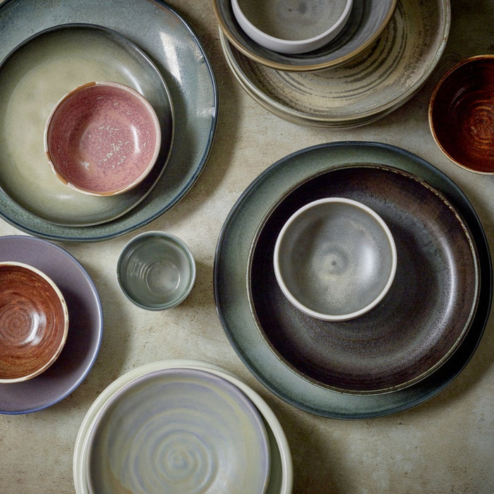 flat lay of green, grey, black, purple, pink and brown plates and bowls made from hotel porcelain