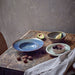 table with a blue pasta plate and green side bowl deep plate with small pink bowl on top filled with walnuts
