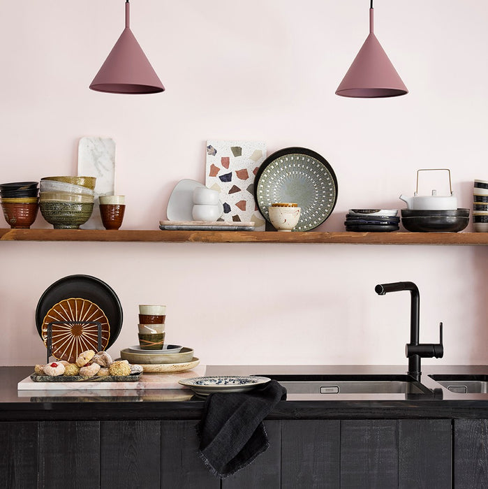 kitchen with two metal triangle shaped pendant lights in a blush color, black cabinets and open shelving with colored ceramics in earth tones