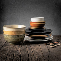 noodle bowls, black and brown dinner and side plates and ceramic teaspoons on a wooden table