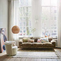 living room with large windows and a brown sofa and a handwoven black and white striped rug on a wooden floor