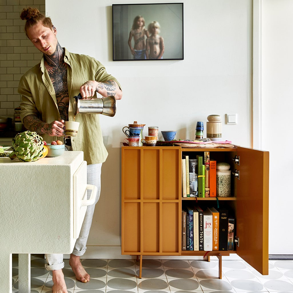 orange credenza filled with retro style 70s ceramics and a man poring coffee in a mug