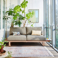 patio with pastel colored sofa, big plants and a muted colored rug