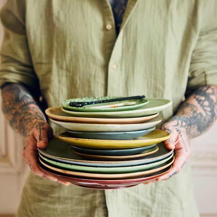 tattooed man holding a stack of stoneware plates in green, orange yellow and greene